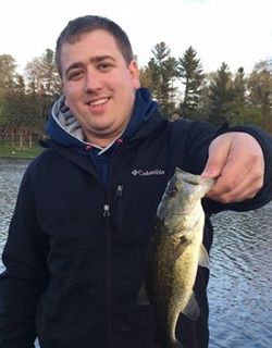 Man in a dark jacket holding a fish. Trees in background.