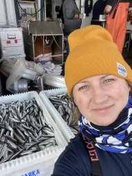 A person in a yellow winter hat. They are smiling. There are small fish in a bin plus other supplies in the background.