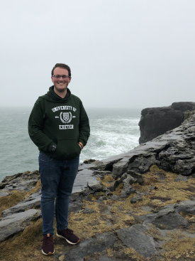 Clayton Hicks wearing a Exeter hoodie poses along the coast of England with a cliff in the background