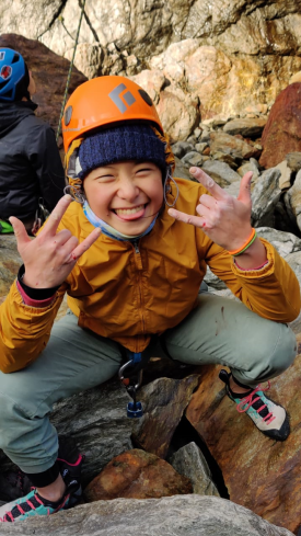 Irena Wong, wearing a helmet and rappelling gear, poses and smiles while rock climbing