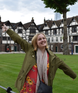 Kara Anderson spreads her arms wide and smiles in front of brown and white houses