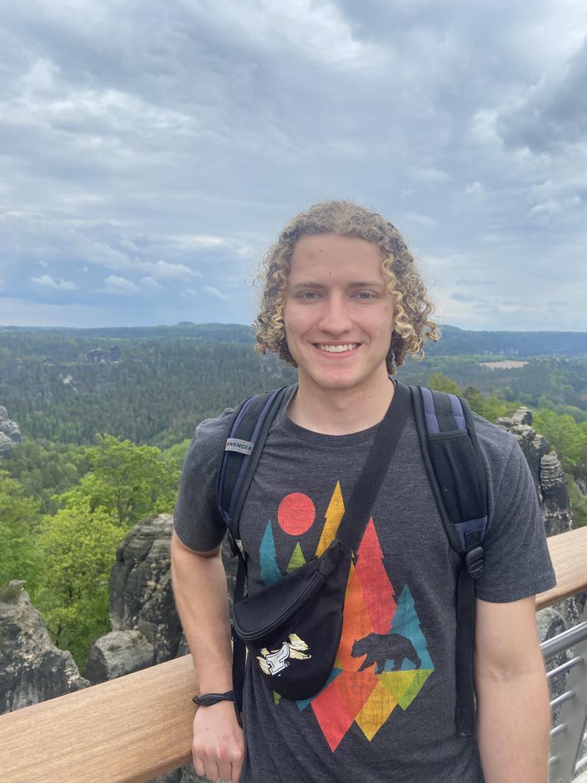 Grant Fiedler stands at a scenic viewpoint with a forest background
