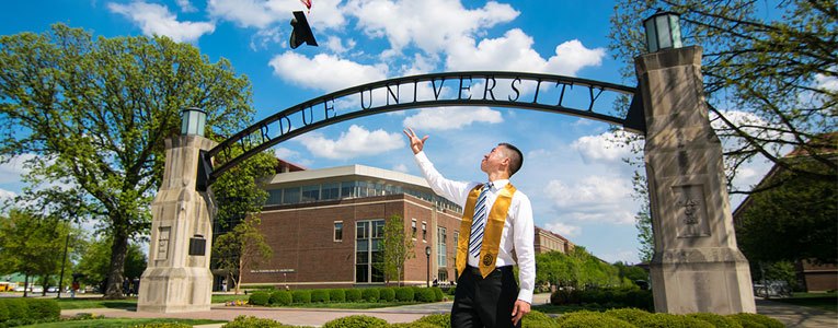 graduate tossing cap in front of gateway arch