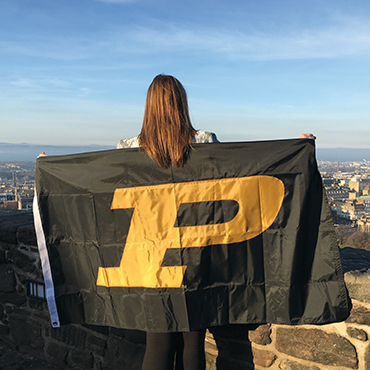 Lydia Pottschmidt draped with a Purdue flag overlooking Edinburgh