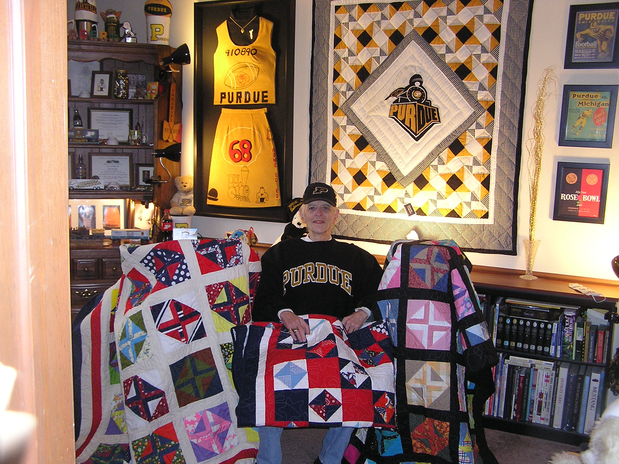 Roger Johnson sits in his home’s Purdue room with three of the quilts he made in memory of his wife, Vicki.