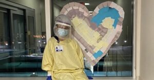 Kaley Anderson is in her PPE gear posing in front of a heart decoration.
