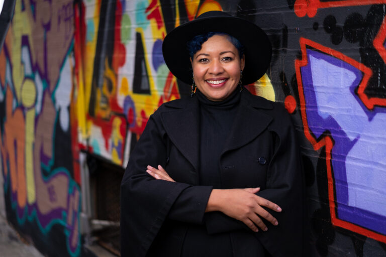 Bianca Pryor poses for a picture in front of a wall with graffiti.