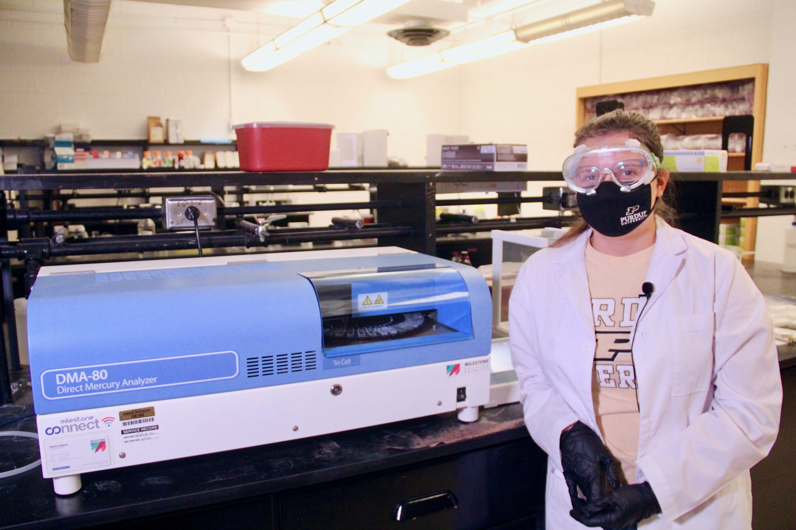 Kiara Smith poses in front of a mercury analyzer machine in a lab.