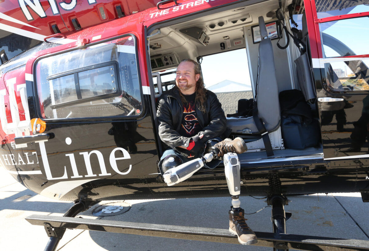 Jeremy Warriner, equipped with robotic legs, sits in the doorway of an IU Health life-line helicopter.