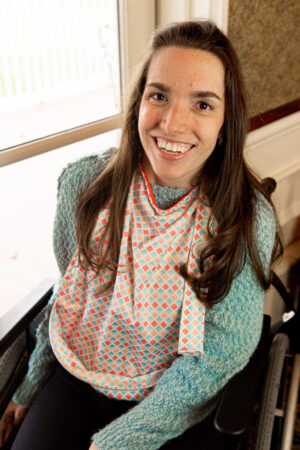 A young woman in a wheelchair wears a pink-and-blue patterned bonTop