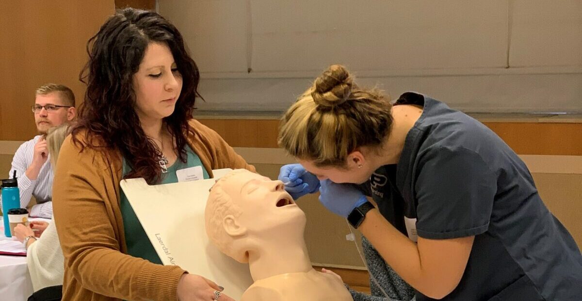 A nursing student inserts a feeding tube into the nose of a simulation dummy.