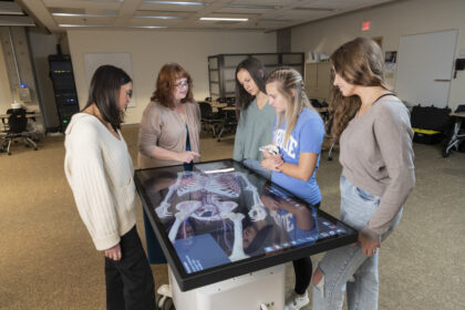 Lisa Hilliard shows three students how to work an Anatomage Clinical Table.