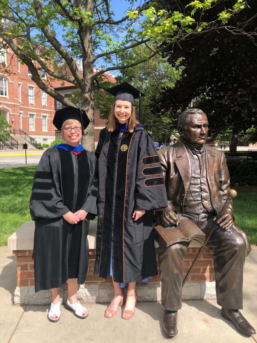 Kim Buhman and Alyssa Zembroski stand in their graduation robes next to the John Purdue statue in Memorial Mall