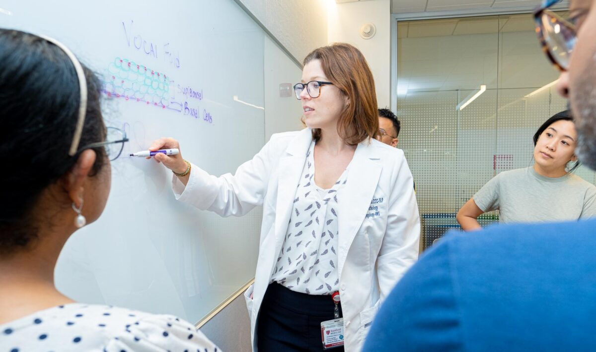 Erickson-DiRenzo writes on a whiteboard in a white labcoat