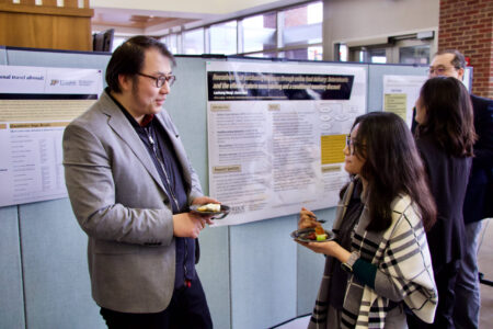 Two individuals stand next to a research poster and chat