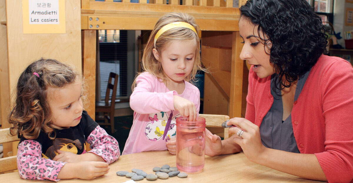 Two young girls work with a staff member on a science experiment with stones and water