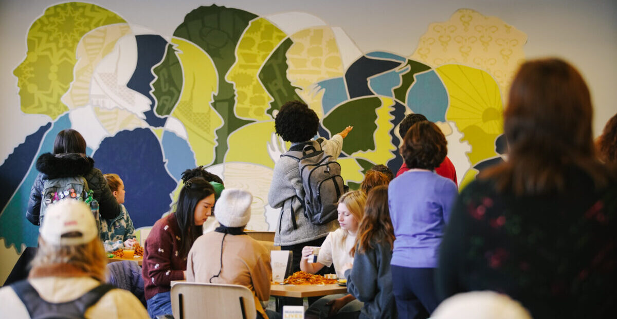 One person stands in the middle of a group and points toward the mural.