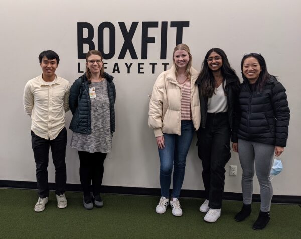 Xu and students pose for a photo next to the BoxFit Lafayette logo