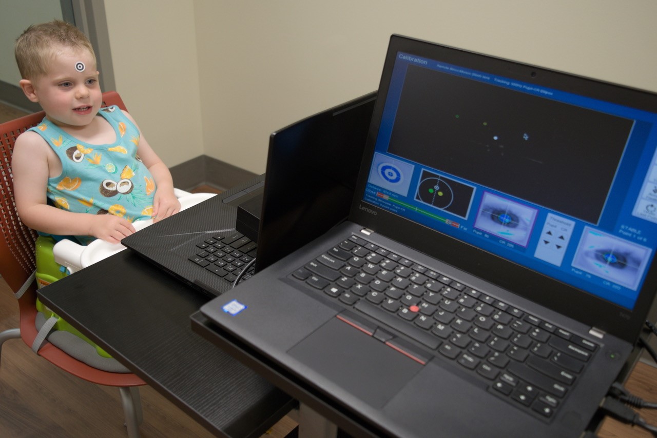 A toddler sits at a table, ready to look at images on a screen.