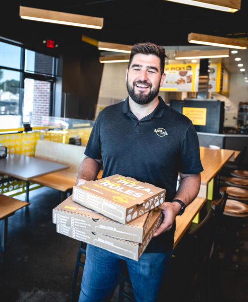 Brad Niemeier stands in an Azzip Pizza location holding pizza boxes