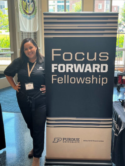 Maya stands next to a "Focus Forward Fellowship" banner