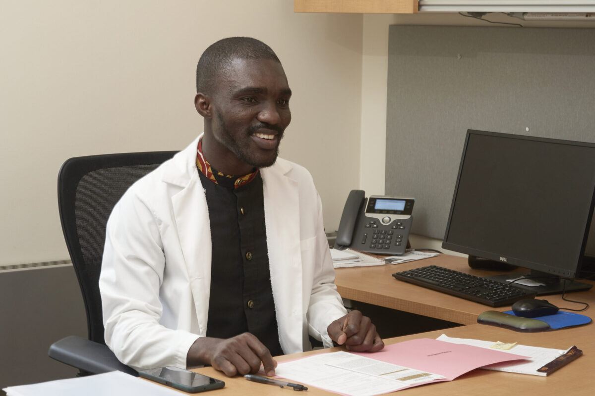 Evans Appiah Osei sits behind a desk, wearing a white coat and smiling