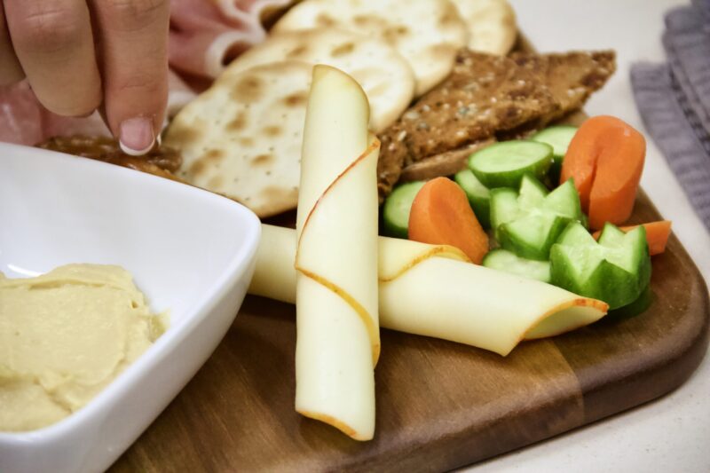 A close shot of cheese, crackers, vegetables and hummus on a charcuterie board.