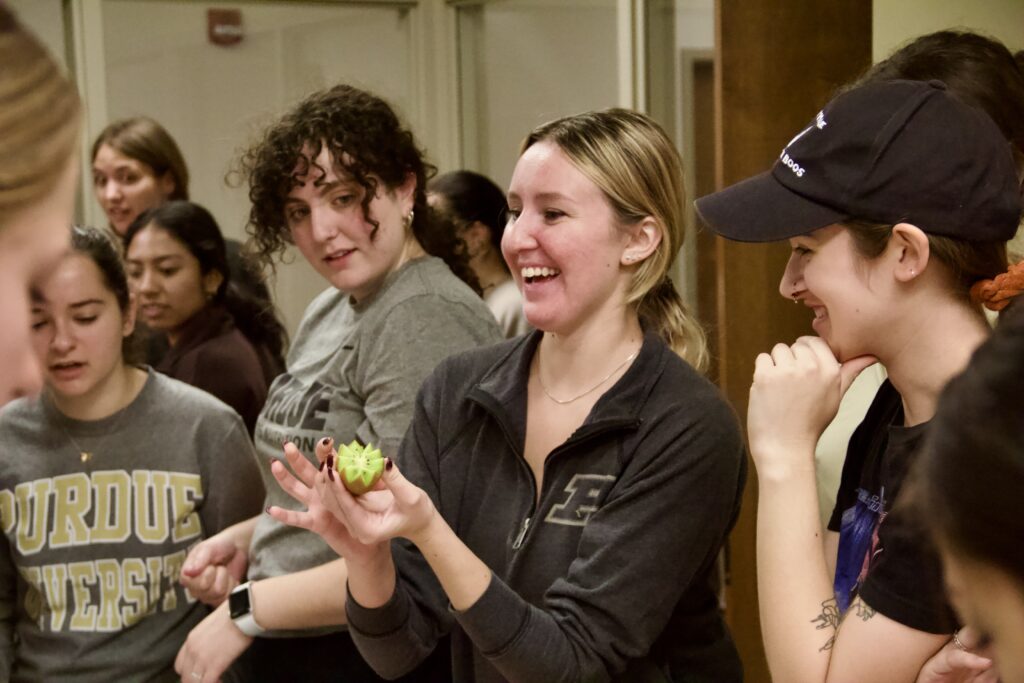 A student proudly holds her chopped kiwi in a class.