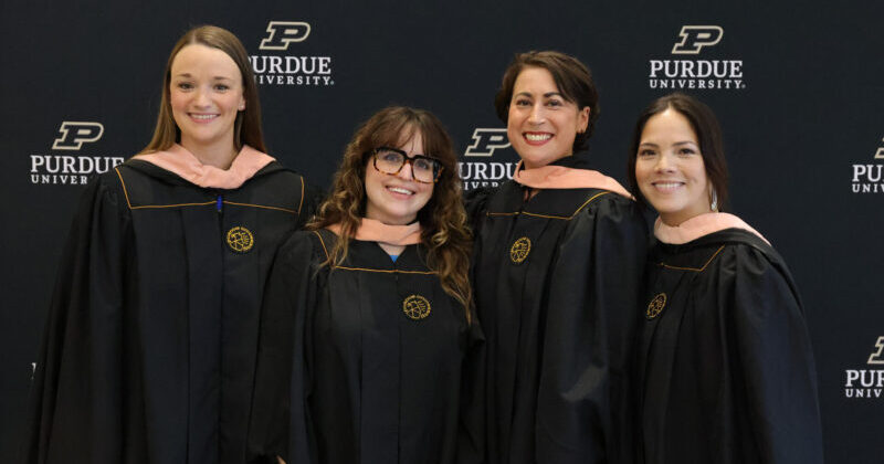 Four women pose together, smiling, in graduation gowns.