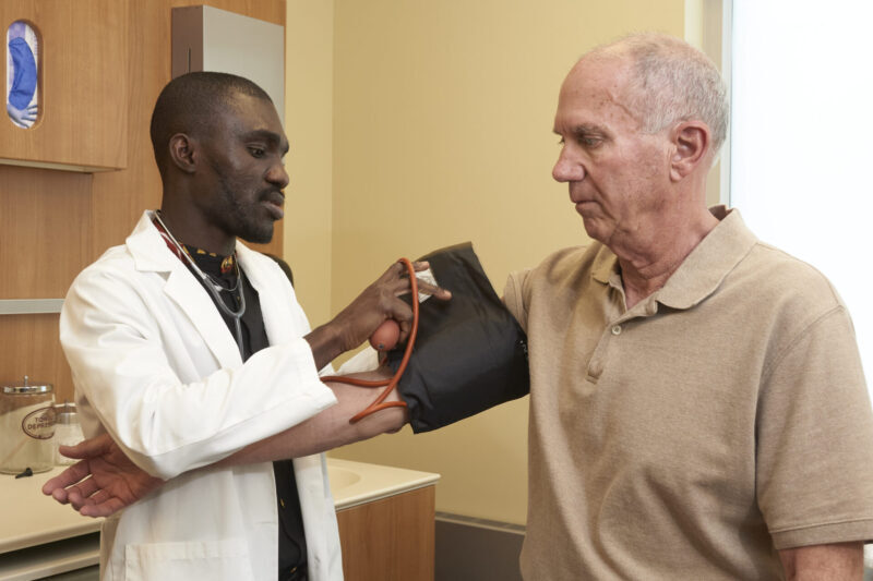 A man in a lab coat takes the blood pressure of an older man.