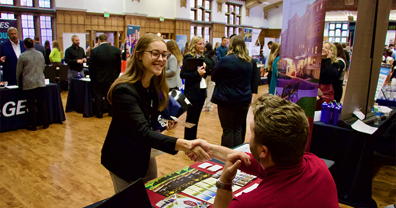 A student shakes hands with a recruiter at a career fair.