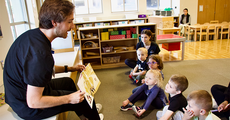 A male graduate student reads to a group of children.