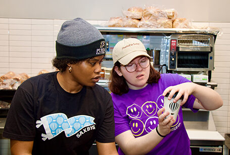 Two women look closely at a coffee cup as they serve guests behind a service counter.