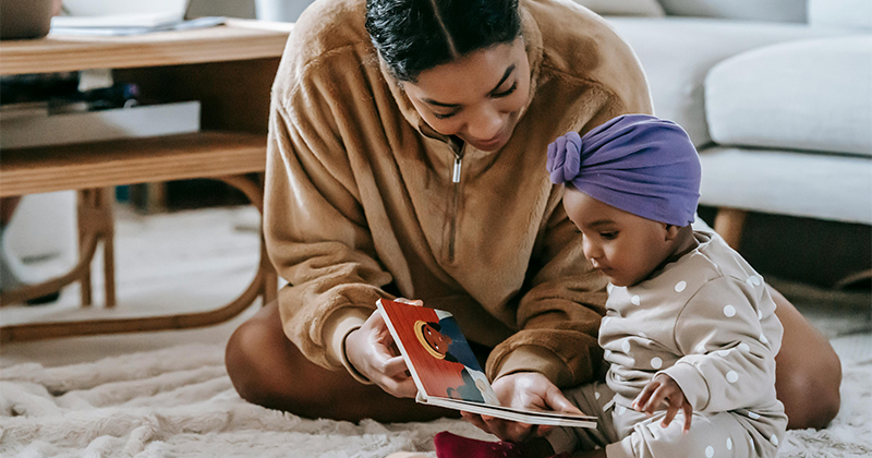 A mother holds a book in front of her baby, who looks at it intently.