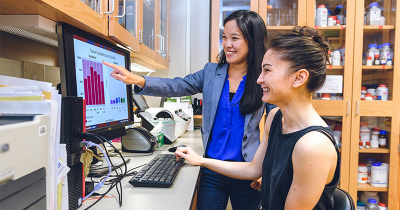 Tzu-Wen Cross points at a computer screen showing something to another woman.