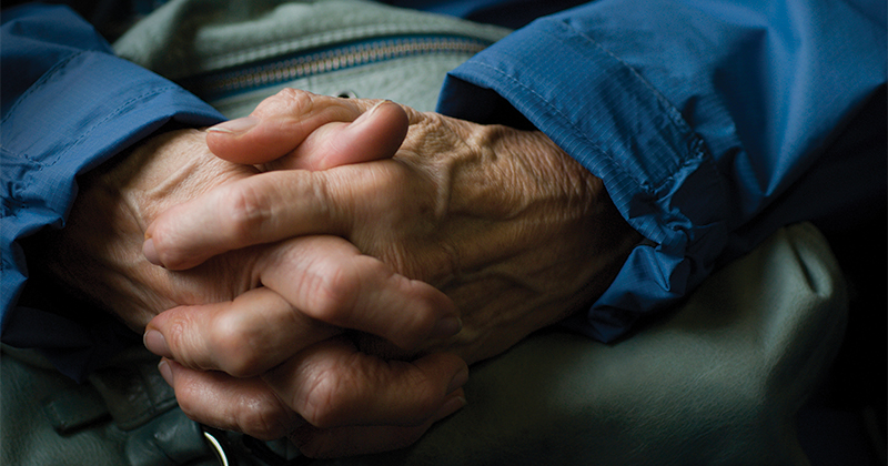 An older adult's hands are folded together.