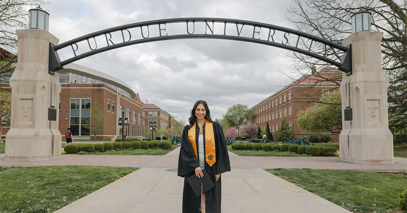 Emily Deldar stands in front of a "Purdue University" arch in her graduation gown.