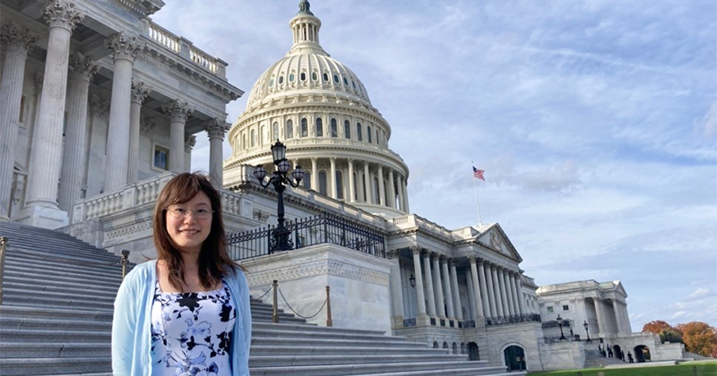 A woman stands on the steps in front of the U.S. Capitol building, smiling.