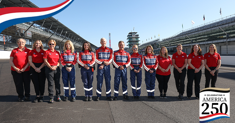 A group of medical team members dressed in red and black outfits line up along the Indianapolis Motor Speedway track for a group picture.