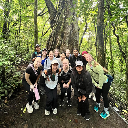 A group of students pose for a photo in a forest, smiling.