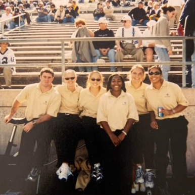 A group of students wearing black pants and polos smile for a photo.