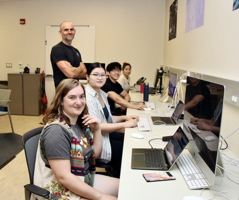 Brandon Keehn stands over his seated students in his lab.