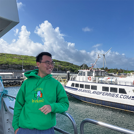 Caleb Siekwandy wears an Ireland sweatshirt on a boat, smiling.