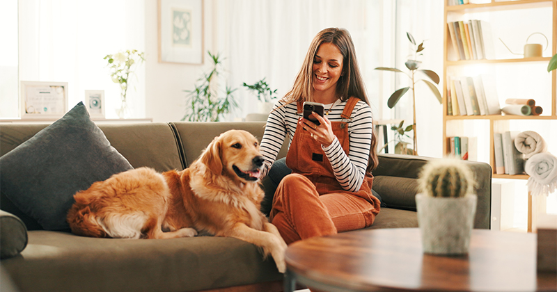 A woman sits on a couch with a golden retriever.