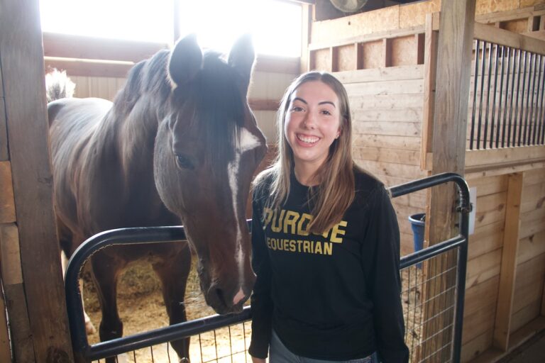 Haylie Johnson poses for a picture with a horse in a stable.