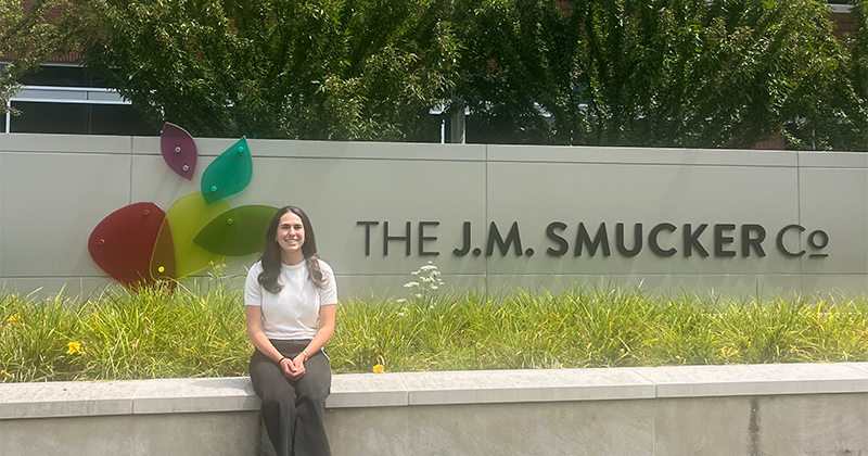 Galit Beraja sits on a concrete ledge next to the J.M. Smucker Co. sign.