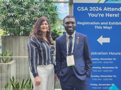 Evans Osei stands with his reearch advisor outside in front of a sign for a conference.