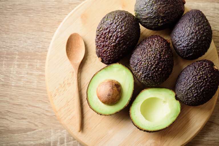 Ripe hass avocado fruit with spoon on wooden plate
