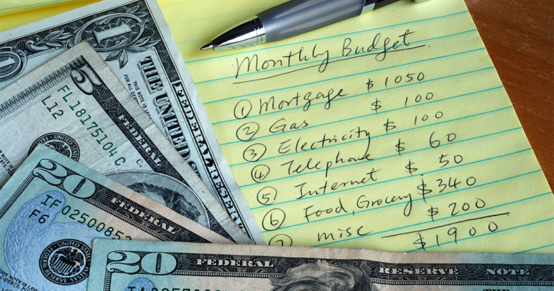 A stock image of money and a piece of paper that breaks down expenses for a monthly budget.