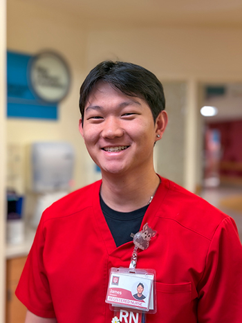 James Shepard smiles wearing his read nursing scrubs